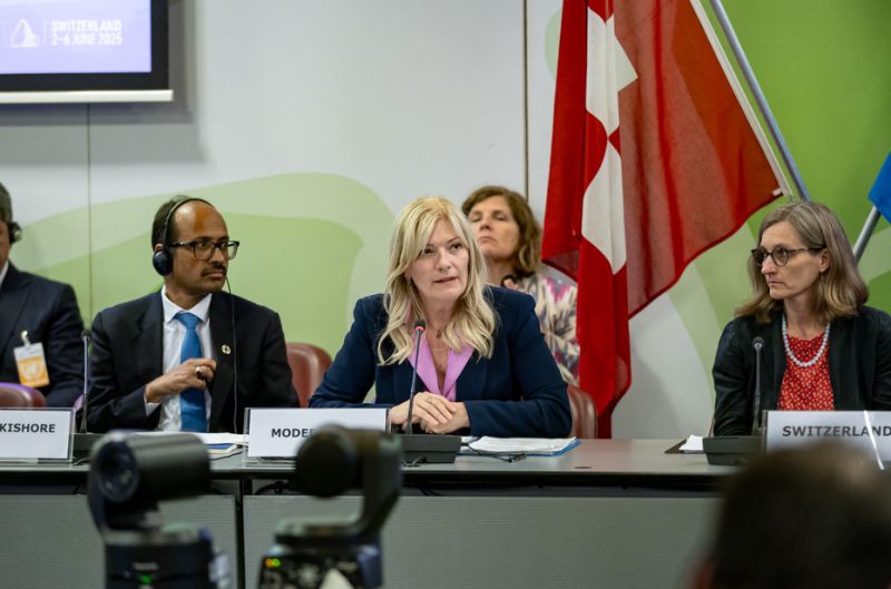 Tre persone sedute a un tavolo di conferenza con microfoni, alle loro spalle le bandiere della Svizzera e dell'Unione Europea.